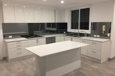 Design ideas for a large modern u-shaped eat-in kitchen in Sydney with a drop-in sink, flat-panel cabinets, white cabinets, quartz benchtops, black splashback, glass sheet splashback, stainless steel appliances, ceramic floors, with island, grey floor and white benchtop.