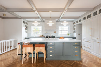 Example of a mid-sized transitional l-shaped medium tone wood floor and brown floor enclosed kitchen design in Salt Lake City with shaker cabinets, white cabinets, an island, white backsplash, subway tile backsplash and stainless steel appliances