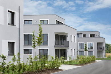Modelo de fachada de piso gris moderna de tres plantas con tejado plano y revestimiento de estuco
