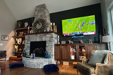 Inspiration for an open concept medium tone wood floor, brown floor and vaulted ceiling family room remodel in Other with black walls, a standard fireplace, a stacked stone fireplace and a wall-mounted tv