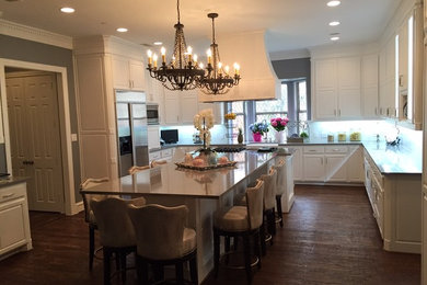 Example of a large classic l-shaped dark wood floor eat-in kitchen design in Dallas with a farmhouse sink, raised-panel cabinets, white cabinets, quartzite countertops, white backsplash, porcelain backsplash, stainless steel appliances and an island