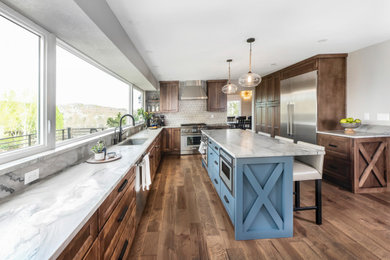 This is an example of a large country l-shaped kitchen/diner in Denver with a submerged sink, raised-panel cabinets, medium wood cabinets, quartz worktops, blue splashback, marble splashback, stainless steel appliances, dark hardwood flooring, an island, brown floors and white worktops.