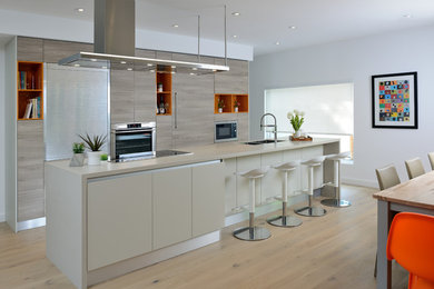 This is an example of a mid-sized contemporary single-wall eat-in kitchen in Toronto with a double-bowl sink, flat-panel cabinets, light wood cabinets, quartzite benchtops, panelled appliances, light hardwood floors, with island and beige floor.