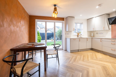 Photo of a medium sized contemporary u-shaped kitchen/diner in Cambridgeshire with a submerged sink, flat-panel cabinets, grey cabinets, quartz worktops, white splashback, black appliances, vinyl flooring, no island, brown floors, white worktops and a feature wall.