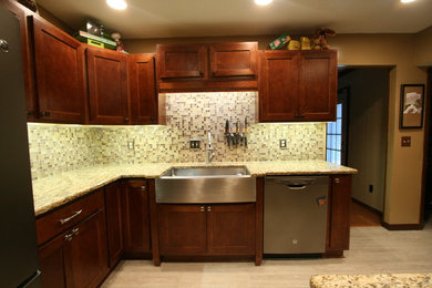 Inspiration for a mid-sized contemporary l-shaped porcelain tile eat-in kitchen remodel in Jacksonville with a farmhouse sink, shaker cabinets, brown cabinets, granite countertops, beige backsplash, glass tile backsplash, stainless steel appliances and no island