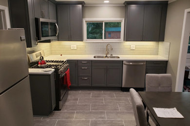Minimalist l-shaped gray floor and vinyl floor eat-in kitchen photo in Other with an undermount sink, shaker cabinets, gray cabinets, solid surface countertops, gray backsplash, glass tile backsplash, stainless steel appliances, no island and white countertops