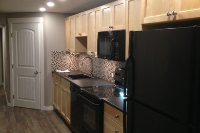 Example of a transitional single-wall medium tone wood floor kitchen design in Calgary with a drop-in sink, recessed-panel cabinets, light wood cabinets, multicolored backsplash, glass tile backsplash and black appliances