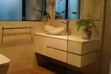 Photo of a small modern 3/4 bathroom in Perth with shaker cabinets, white cabinets, a corner shower, a one-piece toilet, beige tile, ceramic tile, beige walls, porcelain floors, a vessel sink and engineered quartz benchtops.