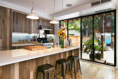 Large beach style galley open plan kitchen in New York with medium wood cabinets, quartz benchtops, blue splashback, porcelain splashback, with island, a farmhouse sink, stainless steel appliances and light hardwood floors.