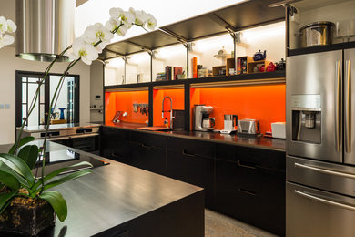 Inspiration for a large contemporary l-shaped open plan kitchen in Perth with a double-bowl sink, flat-panel cabinets, black cabinets, orange splashback, stainless steel appliances, linoleum floors, with island and black benchtop.