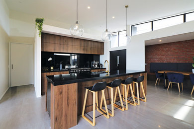 Design ideas for a modern kitchen in Christchurch with flat-panel cabinets, medium wood cabinets, solid surface benchtops, black splashback, with island and black benchtop.