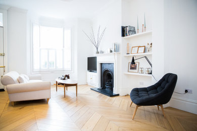 Photo of a medium sized modern formal enclosed living room in London with white walls, light hardwood flooring, a standard fireplace, a metal fireplace surround, a freestanding tv and brown floors.