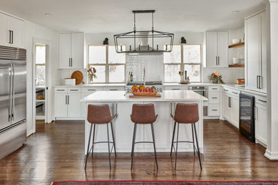 Inspiration for a mid-sized transitional u-shaped medium tone wood floor and brown floor kitchen pantry remodel in Dallas with a farmhouse sink, shaker cabinets, white cabinets, quartzite countertops, white backsplash, stone tile backsplash, stainless steel appliances, an island and white countertops