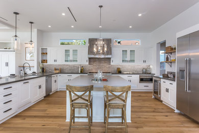 Inspiration for a country u-shaped kitchen in Los Angeles with an undermount sink, shaker cabinets, white cabinets, stainless steel appliances, medium hardwood floors, with island, brown floor and grey benchtop.