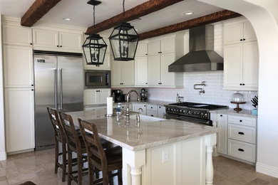 Large tuscan l-shaped marble floor and beige floor open concept kitchen photo in Las Vegas with a farmhouse sink, shaker cabinets, white cabinets, quartzite countertops, white backsplash, ceramic backsplash, stainless steel appliances, an island and multicolored countertops