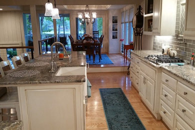 Inspiration for a large transitional galley light wood floor eat-in kitchen remodel in Houston with a farmhouse sink, raised-panel cabinets, distressed cabinets, granite countertops, gray backsplash, porcelain backsplash, stainless steel appliances and an island