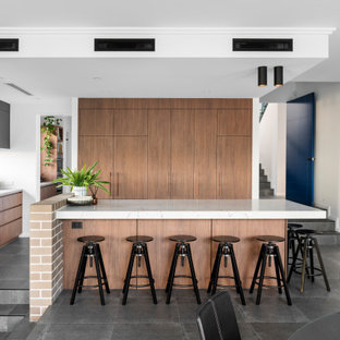 This is an example of a large contemporary l-shaped open plan kitchen in Perth with an undermount sink, flat-panel cabinets, medium wood cabinets, window splashback, panelled appliances, with island, grey floor and white benchtop.