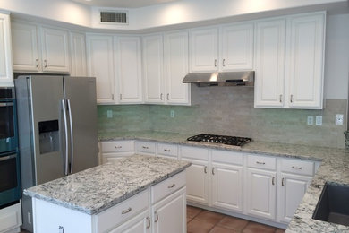 Kitchen - mid-sized traditional u-shaped terra-cotta tile kitchen idea in San Diego with an undermount sink, raised-panel cabinets, white cabinets, granite countertops, beige backsplash, stone tile backsplash, stainless steel appliances and an island
