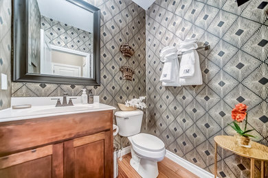 Inspiration for a small contemporary medium tone wood floor and wallpaper powder room remodel in St Louis with shaker cabinets, medium tone wood cabinets, a one-piece toilet, a wall-mount sink, marble countertops, white countertops and a freestanding vanity
