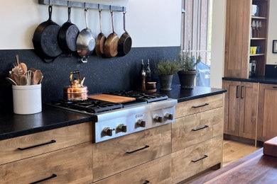 Eat-in kitchen - large transitional galley medium tone wood floor and brown floor eat-in kitchen idea in Other with an undermount sink, flat-panel cabinets, medium tone wood cabinets, quartzite countertops, black backsplash, quartz backsplash, stainless steel appliances, an island and black countertops