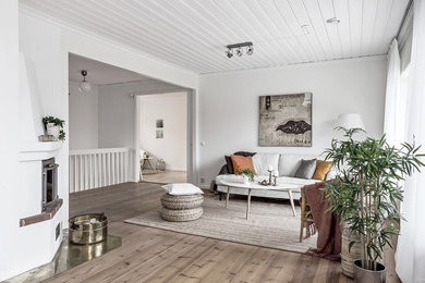 This is an example of a mid-sized scandinavian open concept living room in Stockholm with white walls, light hardwood floors, a corner fireplace, a plaster fireplace surround and no tv.