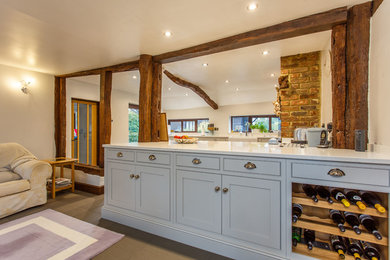 This is an example of a large traditional u-shaped open plan kitchen in Kent with a farmhouse sink, shaker cabinets, grey cabinets, quartzite benchtops, black splashback, glass sheet splashback, panelled appliances, porcelain floors, with island, grey floor and white benchtop.