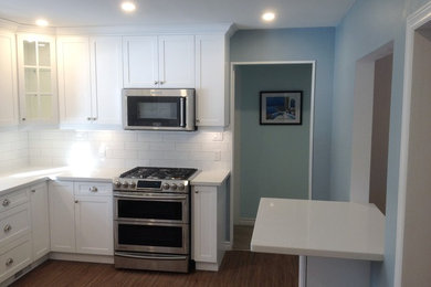 Kitchen in Toronto with a submerged sink, white cabinets, engineered stone countertops, white splashback, stainless steel appliances, vinyl flooring, a breakfast bar and brown floors.