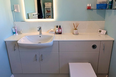Inspiration for a medium sized contemporary family bathroom in West Midlands with flat-panel cabinets, grey cabinets, a corner shower, a one-piece toilet, blue walls, laminate floors, a built-in sink, laminate worktops, brown floors, a sliding door, white worktops, a single sink and a built in vanity unit.
