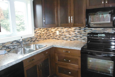 Example of a trendy l-shaped eat-in kitchen design in Vancouver with a drop-in sink, shaker cabinets, medium tone wood cabinets, granite countertops, multicolored backsplash, ceramic backsplash and black appliances