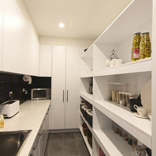 Cette image montre une grande arrière-cuisine minimaliste en L avec un évier posé, un placard à porte plane, des portes de placard blanches, un plan de travail en quartz modifié, une crédence noire, une crédence en carreau de porcelaine, un électroménager en acier inoxydable et un sol en carrelage de porcelaine.