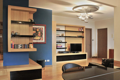 Modelo de biblioteca en casa abierta actual de tamaño medio con paredes azules, suelo de madera en tonos medios y televisor independiente