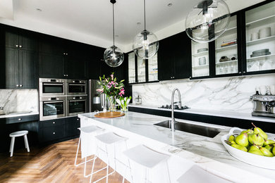 Design ideas for a contemporary l-shaped kitchen in Melbourne with black cabinets, marble benchtops, white splashback, stone slab splashback, stainless steel appliances and medium hardwood floors.