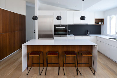 Trendy medium tone wood floor kitchen photo in Minneapolis with flat-panel cabinets, white cabinets, black backsplash, stainless steel appliances, an island and white countertops