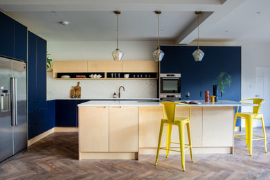 Large contemporary l-shaped open plan kitchen in London with a built-in sink, flat-panel cabinets, light wood cabinets, quartz worktops, white splashback, ceramic splashback, stainless steel appliances, light hardwood flooring, an island, brown floors, white worktops and a feature wall.