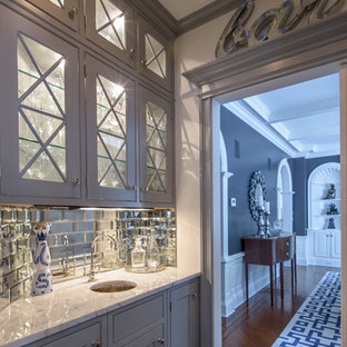 ニューヨークの小さいトランジショナルスタイルのおしゃれなウェットバー (アンダーカウンターシンク、ガラス扉のキャビネット、グレーのキャビネット、大理石カウンター、サブウェイタイルのキッチンパネル、濃色無垢フローリング、グレーのキッチンカウンター) の写真