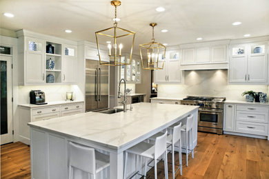 Inspiration for a large transitional l-shaped eat-in kitchen in Chicago with a farmhouse sink, recessed-panel cabinets, white cabinets, quartz benchtops, white splashback, engineered quartz splashback, stainless steel appliances, light hardwood floors, with island, brown floor and white benchtop.