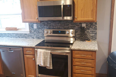 Mid-sized elegant u-shaped eat-in kitchen photo in Other with recessed-panel cabinets, brown cabinets, quartz countertops, multicolored backsplash, stainless steel appliances, a peninsula and multicolored countertops