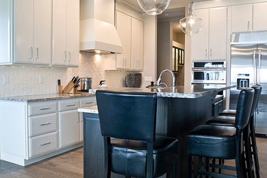 Example of a large trendy l-shaped dark wood floor and brown floor kitchen design in Other with stainless steel appliances, an undermount sink, flat-panel cabinets, white cabinets, granite countertops, white backsplash, ceramic backsplash and an island
