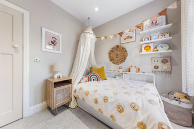 This is an example of a small eclectic gender neutral toddler’s room in London with beige walls, carpet, beige floors and feature lighting.