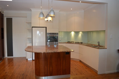 This is an example of a large traditional l-shaped eat-in kitchen in Sydney with white cabinets, granite benchtops, green splashback, glass sheet splashback and with island.