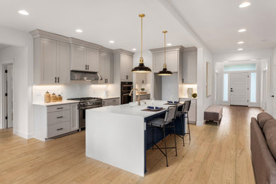 Trendy l-shaped light wood floor and brown floor open concept kitchen photo in Los Angeles with a drop-in sink, flat-panel cabinets, gray cabinets, granite countertops, white backsplash, subway tile backsplash, stainless steel appliances, an island and white countertops