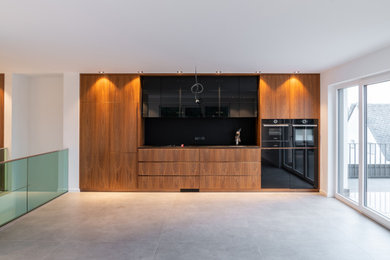Offene Moderne Küche in grau-weiß in L-Form mit flächenbündigen Schrankfronten, dunklen Holzschränken, Küchenrückwand in Schwarz und Keramikboden in Sonstige