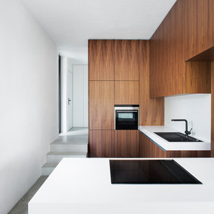 Пример оригинального дизайна интерьера: маленькая отдельная кухня в стиле модернизм с плоскими фасадами, фасадами цвета дерева среднего тона, полуостровом, накладной раковиной, белым фартуком, техникой под мебельный фасад, бетонным полом и серым полом