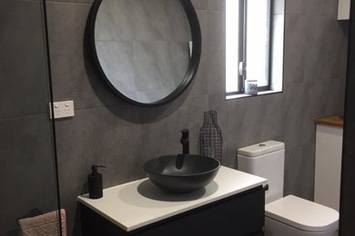 Photo of a contemporary 3/4 bathroom in Brisbane with flat-panel cabinets, black cabinets, a corner shower, gray tile, porcelain tile, grey walls, porcelain floors, a vessel sink, engineered quartz benchtops, a hinged shower door and white benchtops.