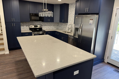 Example of a mid-sized trendy l-shaped vinyl floor eat-in kitchen design in Other with an undermount sink, shaker cabinets, blue cabinets, quartz countertops, multicolored backsplash, ceramic backsplash, stainless steel appliances, an island and gray countertops