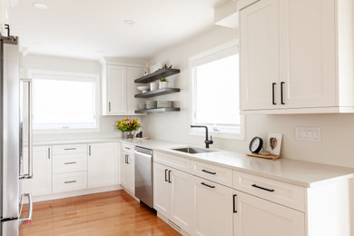 Eat-in kitchen - mid-sized transitional u-shaped light wood floor and brown floor eat-in kitchen idea in Toronto with an undermount sink, shaker cabinets, white cabinets, quartz countertops, white backsplash, stainless steel appliances, no island and white countertops