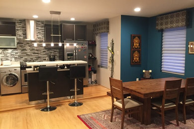 Example of a small eclectic single-wall light wood floor and beige floor open concept kitchen design with flat-panel cabinets, black cabinets, quartz countertops, multicolored backsplash, matchstick tile backsplash, stainless steel appliances and an island