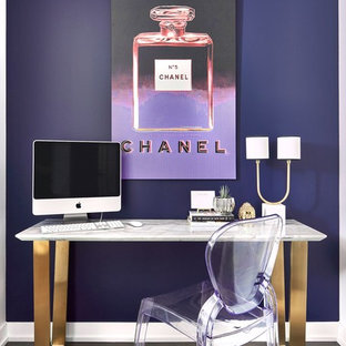 Modern inredning av ett litet hemmabibliotek, med lila väggar, mörkt trägolv, ett fristående skrivbord och brunt golv