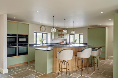 Design ideas for a large contemporary l-shaped kitchen in Gloucestershire with flat-panel cabinets, granite worktops, black appliances, an island, black worktops, a single-bowl sink, green cabinets and brown floors.