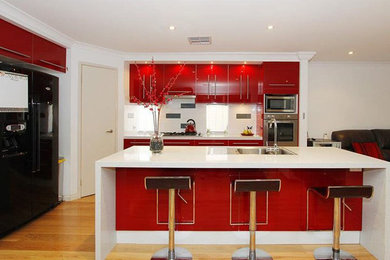 Mid-sized trendy galley medium tone wood floor enclosed kitchen photo in DC Metro with a drop-in sink, flat-panel cabinets, red cabinets, quartz countertops, white backsplash, ceramic backsplash, stainless steel appliances and an island